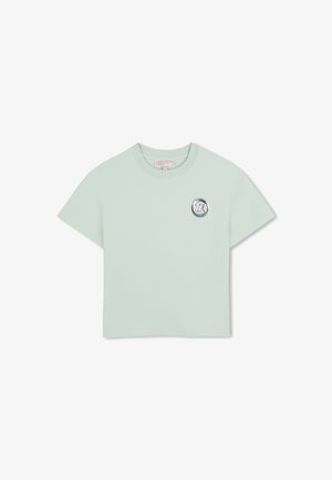 T-shirt court à manches courtes vert clair avec un col rond et un petit logo circulaire argenté MK sur la poitrine gauche.