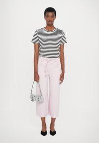 T-shirt a righe bianco e nere, jeans a gamba larga rosa chiaro con coulisse, borsa argentata, ballerine nere a punta. Outfit chiaro e casual.