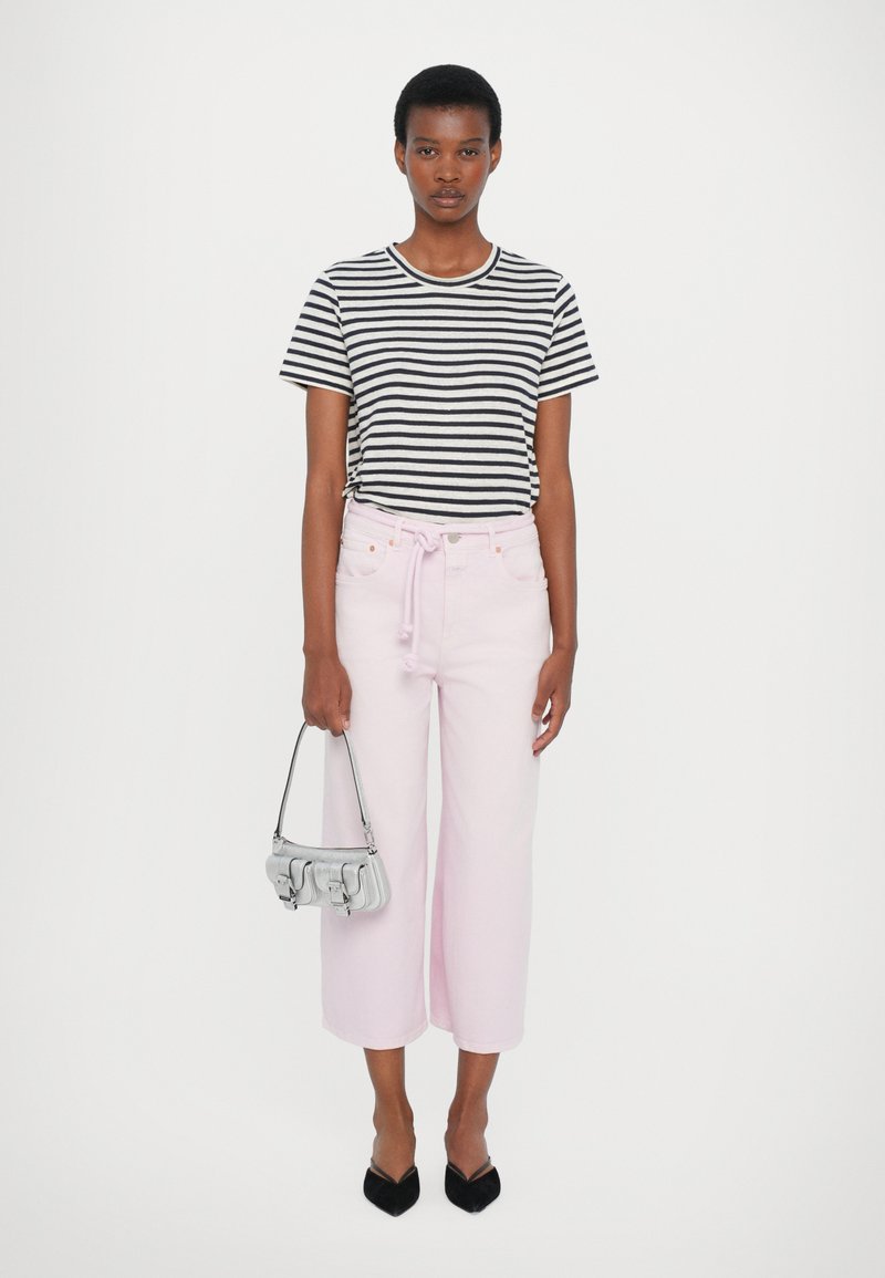 T-shirt a righe bianco e nere, jeans a gamba larga rosa chiaro con coulisse, borsa argentata, ballerine nere a punta. Outfit chiaro e casual.
