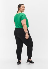 Top verde a maniche corte abbinato a jogger neri attillati e sneakers nere, caratterizzato da una vestibilità rilassata e un design classico con una texture semplice.
