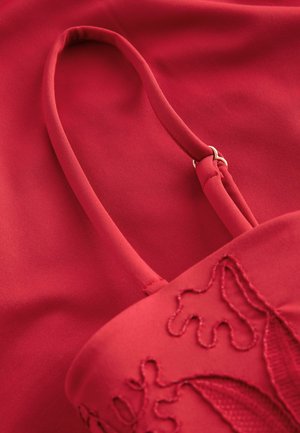 Sac en tissu rouge avec une texture lisse, doté d'une fine sangle et d'un élégant motif floral brodé. La couleur générale est un rouge profond et vibrant.