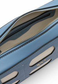 Intérieur d'un sac en cuir bleu clair avec une fermeture éclair dorée et une doublure en tissu contrasté. Présente des motifs découpés à l'extérieur.