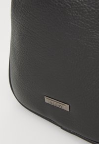 Borsa in pelle nera con texture, finitura liscia e una placca logo metallica. Caratterizzata da bordi arrotondati e un design elegante.