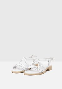 Sandales en cuir blanc avec un design à lanières croisées, ouvertes à l'avant, un petit talon carré et de subtils motifs sur les lanières.