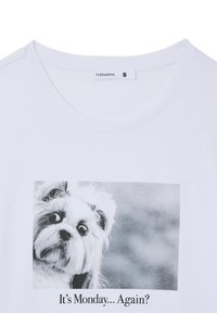 T-shirt di cotone bianco con una stampa in bianco e nero di un cane con occhi grandi, con la didascalia "È lunedì... di nuovo?" sotto l'immagine.