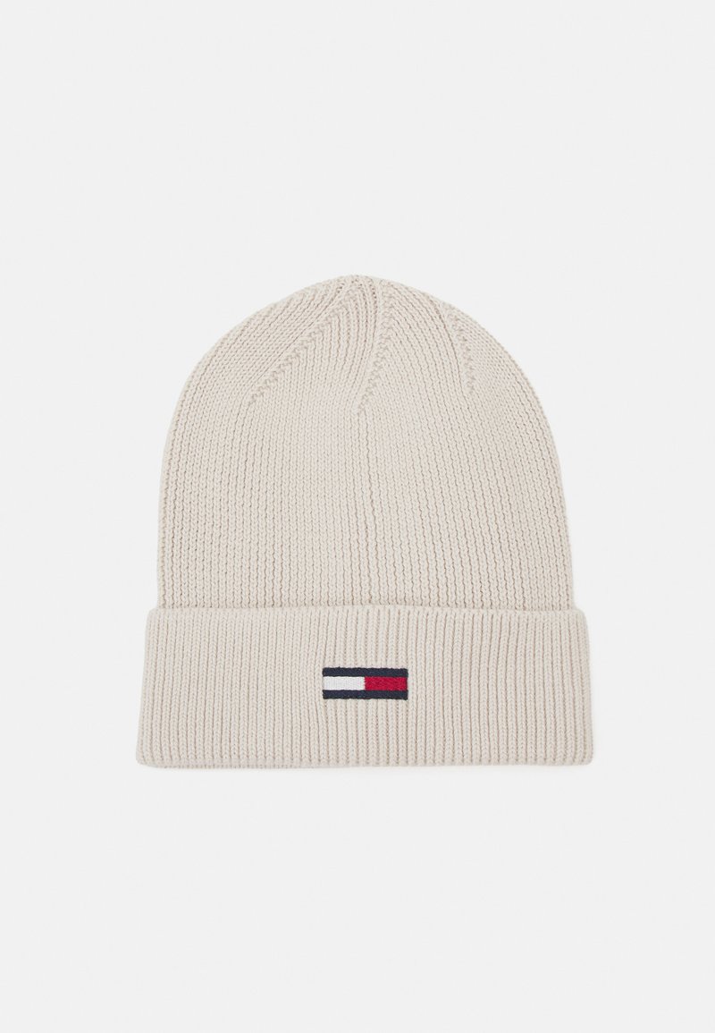 Gorro de punto color crema con vuelta, con un pequeño logo de bandera en rojo, blanco y azul. Tela texturizada y elástica.
