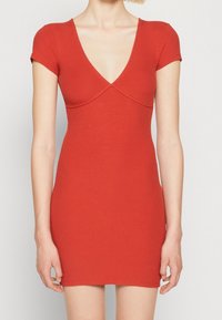 Punainen rahkakuosiset mekko, jossa on syvä V-pääntie ja lyhyet hihat. Muotoonsa leikattu malli korostaa vartalon muotoa, ja siinä on sileä pinta sekä saumaton helma.