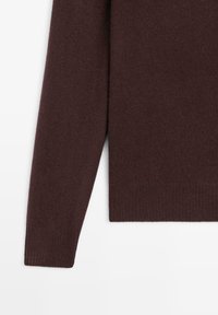 Bordowy sweter z prążkowanej dzianiny, z długim rękawem i zaokrąglonym dołem, wykonany z miękkiego materiału dzianego. Skupienie na detalu rękawa i dolnej części ubrania.