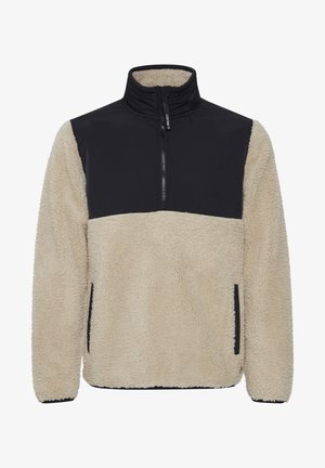 Polarowy polar z wysokim kołnierzem, beżowym korpusem, czarną górną częścią i bocznymi kieszeniami. Teksturowana powierzchnia o miękkim, ciepłym wyglądzie.