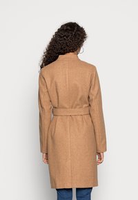 Manteau en laine marron à coupe ajustée, ceinturé à la taille, manches longues et col montant. Texture lisse, longueur jusqu'aux genoux.