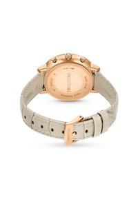 Runder Edelstahl-Uhrenboden mit roségoldener Beschichtung und klarem Kristallakzent. Beigefarbener, krokodilgeprägter Lederarmband mit goldenen Beschlägen.