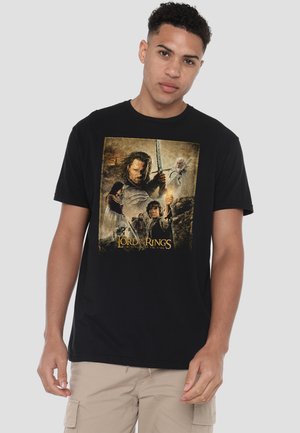Man wearing black t-shirt with Lord of the Rings movie poster print holding a sword, a glowing light, and other characters on the front.