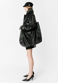 Chaqueta de cuero negra de gran tamaño con acabado texturizado, combinada con una falda corta negra. Los accesorios incluyen una gorra negra y un bolso tote de cuero.