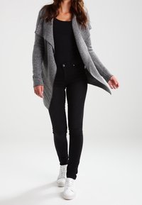 Gray herringbone cardigan with an open front, black top, and black slim jeans. Paired with white sneakers. Smooth fabric and casual design.