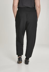 Pantalons noirs légers avec une taille smock élastiquée, des jambes effilées et des poignets élastiques. Portés avec des chaussures noires.