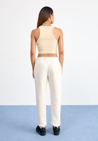 Top de tanque em bege com nervuras combinado com umas calças de moletão brancas. O conjunto apresenta um design cropped, e as calças de moletão têm um cós elástico.