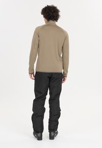 Brauner langärmliger Baselayer mit hohem Kragen, kombiniert mit schwarzen wasserdichten Hosen. Beide Kleidungsstücke weisen dezente Texturen und funktionales Design auf.