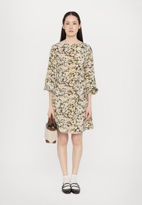Floral dress in light beige with green and pink patterns, bell sleeves, belted waist, paired with a small brown and white bag and dark shoes.
