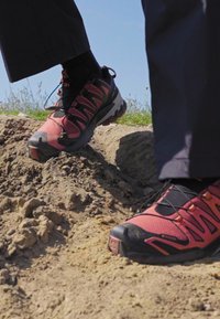 Chaussures de randonnée rouges et noires avec une surface texturée et un motif, dotées d'une semelle robuste, adaptées aux terrains accidentés.