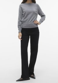 Szary dzianinowy sweter z okrągłym dekoltem, zestawiony z czarnymi rozkloszowanymi spodniami i czarnymi balerinami z ostrym noskiem. Gładka faktura i dopasowany krój.