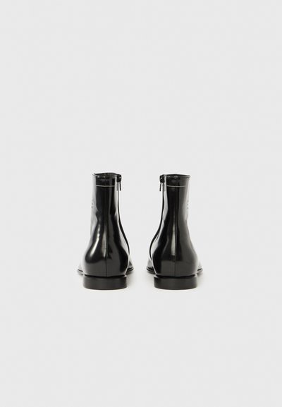 Μαύρα μποτάκια αστραγάλου από πατενταρισμένο δέρμα με ομαλή υφή, που διαθέτουν πλαϊνό φερμουάρ και χαμηλό, στρογγυλεμένο τακούνι.
