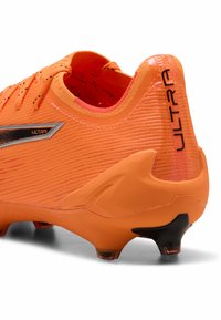 Scarpino da calcio arancione brillante con materiale testurizzato, forma curvata e tacchetti neri. Presenta il marchio "ULTRA" in argento sul lato.