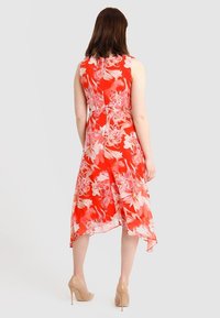 Abito floreale rosso con un design senza maniche, orlo fluente e trama trasparente. Presenta fiori rosa e una chiusura con cerniera sul retro.