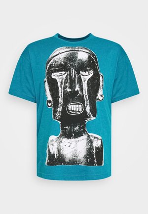 Blaues T-Shirt mit einem großen schwarz-weißen abstrakten Tribal-Gesicht, das tränenähnliche Markierungen und einen grimmig verzogenen Mund zeigt.
