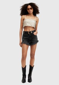 Top corto all'uncinetto di colore avorio, abbinato a pantaloni di jeans neri a vita alta con orli sfrangiati. Cintura nera con fibbia dorata e stivali neri fino al ginocchio.