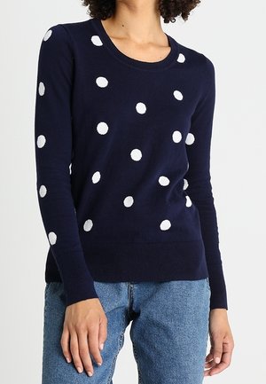 Pull marin à pois blancs, à manches longues, col rond, ourlet côtelé, fabriqué dans un matériau doux, porté avec un jean bleu clair.