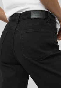 Jean en denim noir au design épuré, doté d'une étiquette en cuir à la taille, de deux poches arrière et de détails de couture subtils.