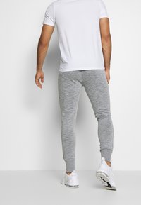 Grå joggebukser med slim fit og ribstrikkede manchetter, parret med en hvid kortærmet skjorte og hvide sportsko.