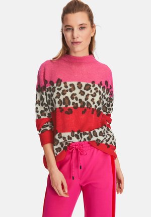 Knit sweater featuring pink and red stripes, leopard print pattern, high neck, and loose fit. Paired with pink joggers.