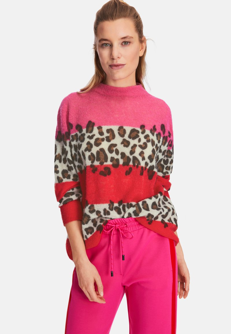 Strickpullover mit rosa und roten Streifen, Leopardenmuster, hohem Kragen und lockerer Passform. Kombiniert mit rosa Jogginghosen.