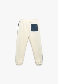 Cremefarvede sweatpants med elastisk talje, marineblå sidedele og en lomme. Lavet af blødt materiale med en afslappet pasform.