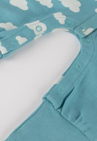 Helles, blaues Kleidungsstück mit weißen Wolkenmustern, mit Druckknopfverschlüssen am Halsausschnitt und einem weichen, strukturierten Stoff.