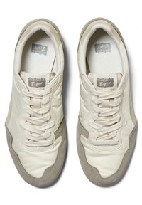 Lys beige sneakers med en glat læderoverdel, grå ruskindsdetaljer, flade hvide snørebånd, rund tå og en tekstureret indersål.