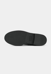 Semelle de chaussure en caoutchouc noir avec une texture lisse, un léger talon et un motif de logo. La forme est arrondie avec une base plate pour la stabilité.