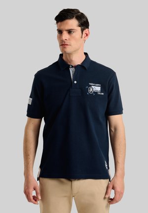 Camisa polo azul marino de algodón, con cuello a rayas blancas, detalles de logo bordados y mangas cortas con aberturas laterales.