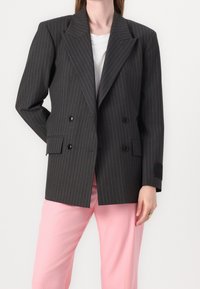Szary żakiet w paski, dwurzędowy, z szerokimi klapami, czarnymi guzikami i dwoma bocznymi kieszeniami, w zestawieniu z jasnoróżowymi spodniami.