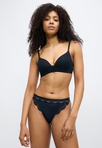 Zwarte beha met naadloze cups en verstelbare bandjes, gecombineerd met een bijpassende zwarte string met kanten accenten en een tailleband met logo.