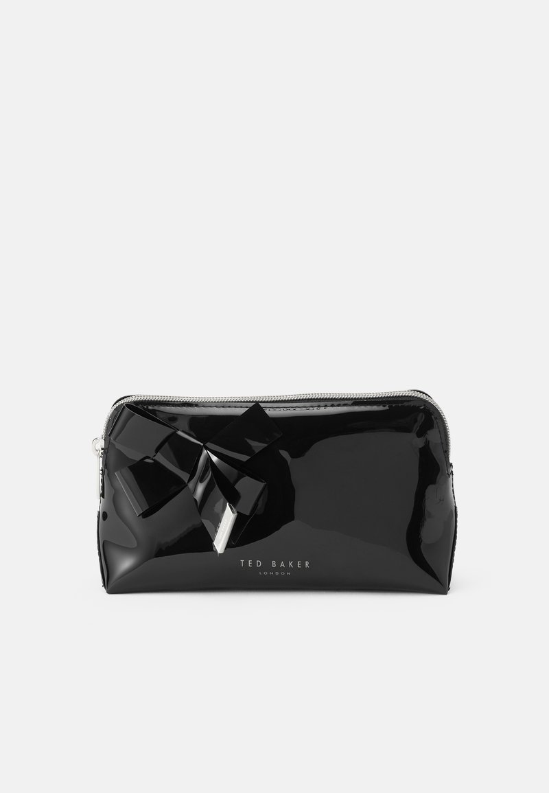 Bolso de charol negro con acabado brillante, que presenta un gran lazo negro como acento y una cremallera plateada. Logotipo "TED BAKER" impreso en la parte inferior.