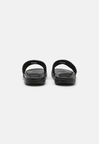 Sandalias negras con plantillas texturizadas y correas anchas y curvas. El material es sintético, con un diseño de punta abierta y sin respaldo.