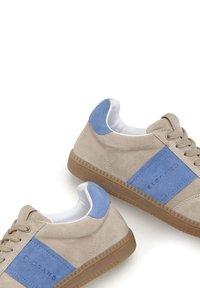 Beige Wildledersneaker mit hellblauen Akzenten, strukturierten Gummisohlen und runder weißer Knöchelpartie. Mit Logo an der Seite und Schnürdesign.