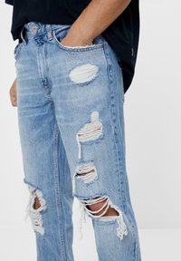 Ljusblå denimjeans med tydliga revor och fransiga kanter, med slitna partier i olika storlekar och en klassisk design med fem fickor.