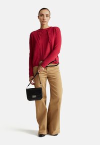 Červený kardigan ze směsi vlny přes odpovídající top, spárovaný s béžovými širokými kalhotami. Černá taška přes rameno z umělé kůže se stříbrnými akcenty.