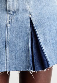 Denimskjørt i lys blått stoff med frayed hem og sidelister. Sølvfarge detaljer ved åpningen av listen gir ekstra preg.