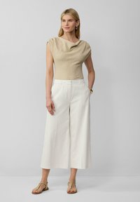 Beige gestructureerde top met wijde hals, gecombineerd met witte wijde broek en tan platte sandalen, ontworpen voor een ontspannen pasvorm.