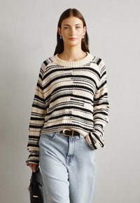 Maglione a righe in crema e nero, texture in maglia, scollatura rotonda ampia e maniche lunghe. Abbinato a jeans azzurri chiari e una borsa nera.