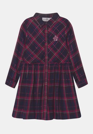 Dunkles, kariertes Kleid mit langen Ärmeln, Kragen, Knopfleiste vorne, Taillenraffung und einem kleinen pinken Paillettenstern auf der Brust.